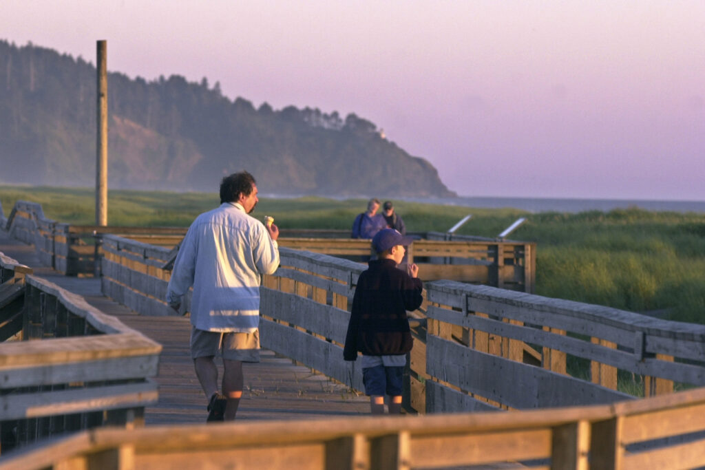 Image of a father and son walking along the beach boardwalk while eating ice cream at sunset.