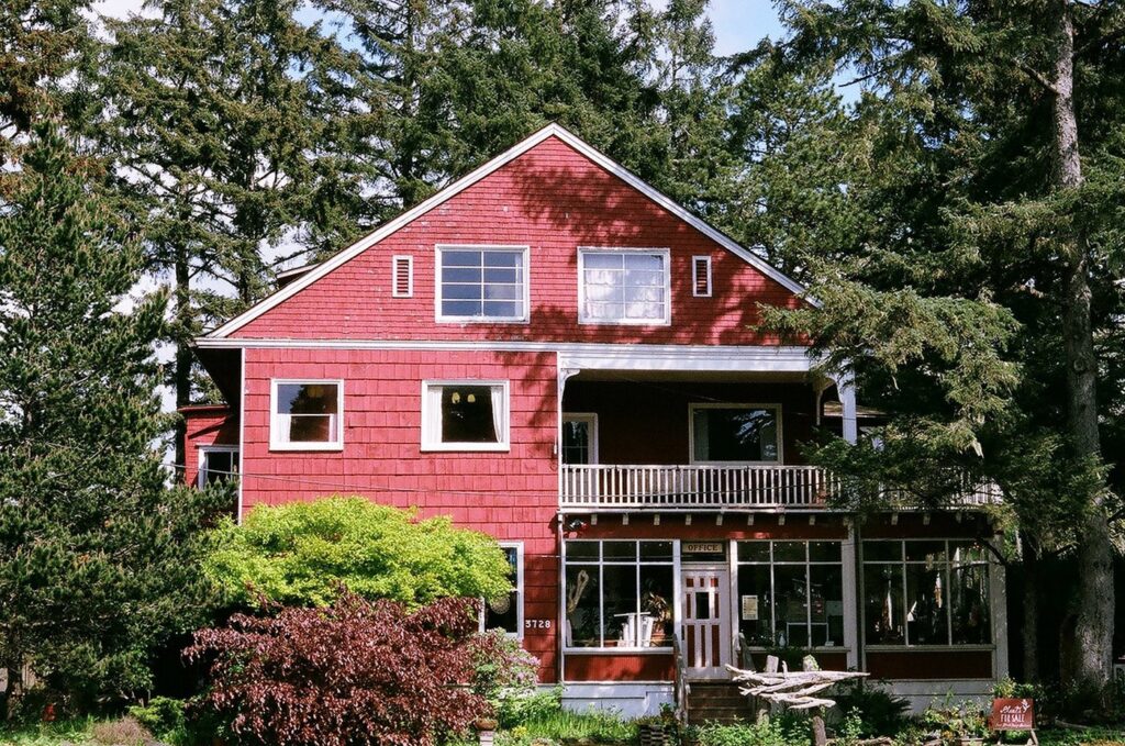 An image of the historic Sou'Wester Lodge with its red siding and white trim, bold situated in a lush forest.