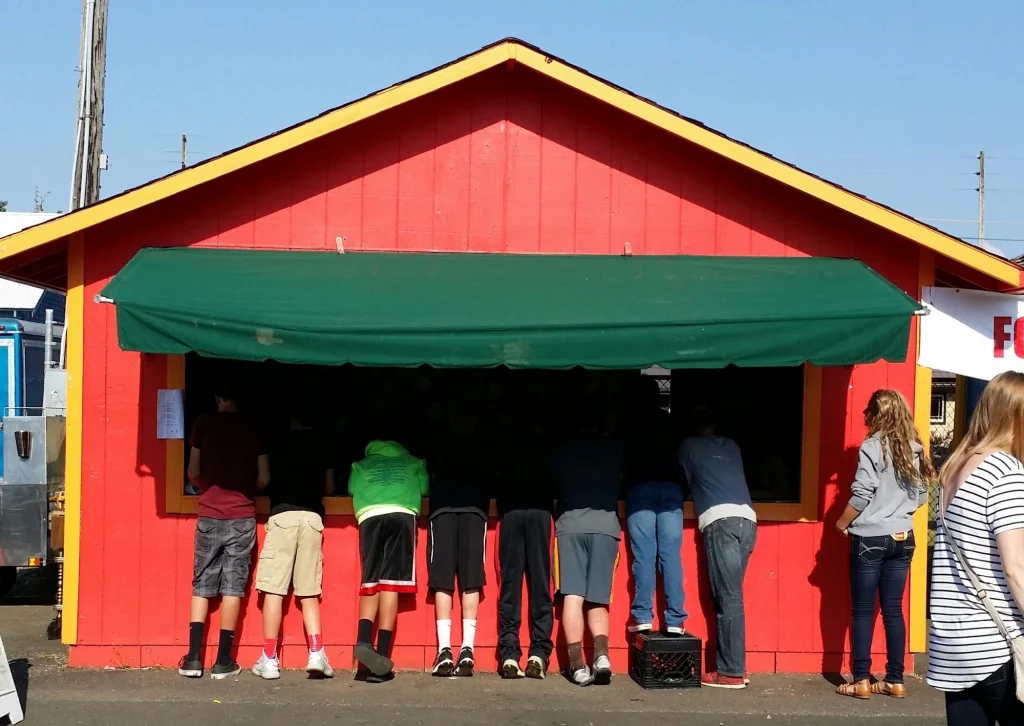 An image of young people lining up at a bright red-painted booth at the County Faire.