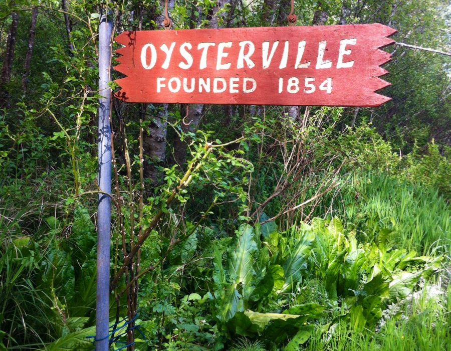 An image of a hand-painted red sign stating, 'Oysterville, Founded in 1854'.