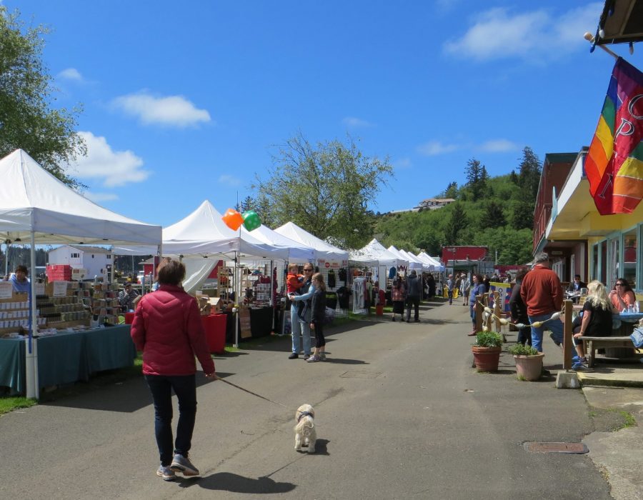 Another image of the local grower's market. This time, the camera pans out to the whole street to show the busy stalls and locals milling about in the sunshine with their families..