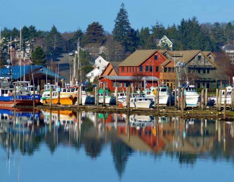 A colorful image of Ilwaco as seen from the lake. The brightly colored boats contrasted with the red buildings and blue water gives the picture an idyllic feeling.