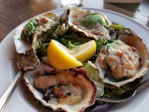 An image of four large oysters artfully presented on a plate with lemon wedges as garnish.