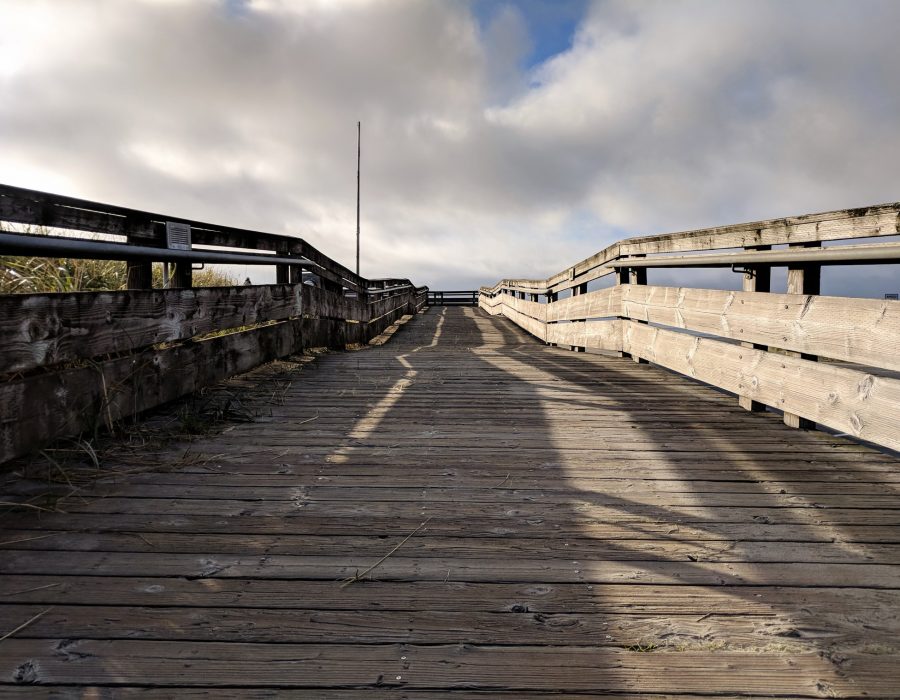 An image of a wide, wooden boardwalk taken from the perspective of a child, making the sky and distance seem much larger.