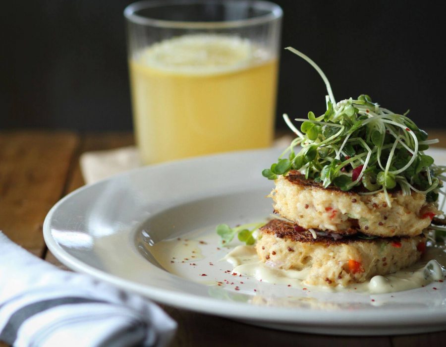 An image of two crab patties delicately placed atop one another with a nest of garnished microgreens to crown them.