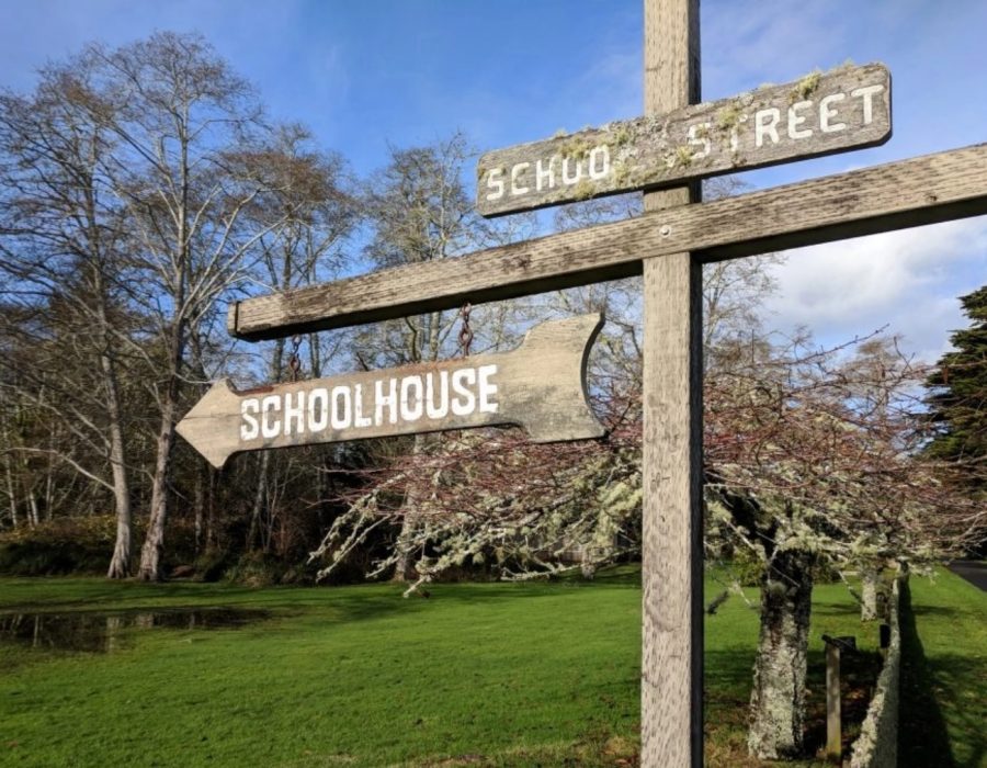 An image of a historic signpost in Oysterville with its typography still legible, pointing the way to the local schoolhouse.
