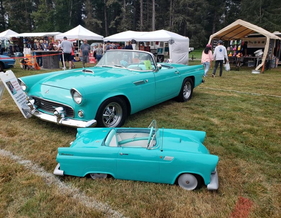An image of one of the cars showcased at the Ocean Park Rod Run of a fancy cerulean blue hotrod - convertible of course, and a mini, exact replica suitable for a child next to it on the grass.