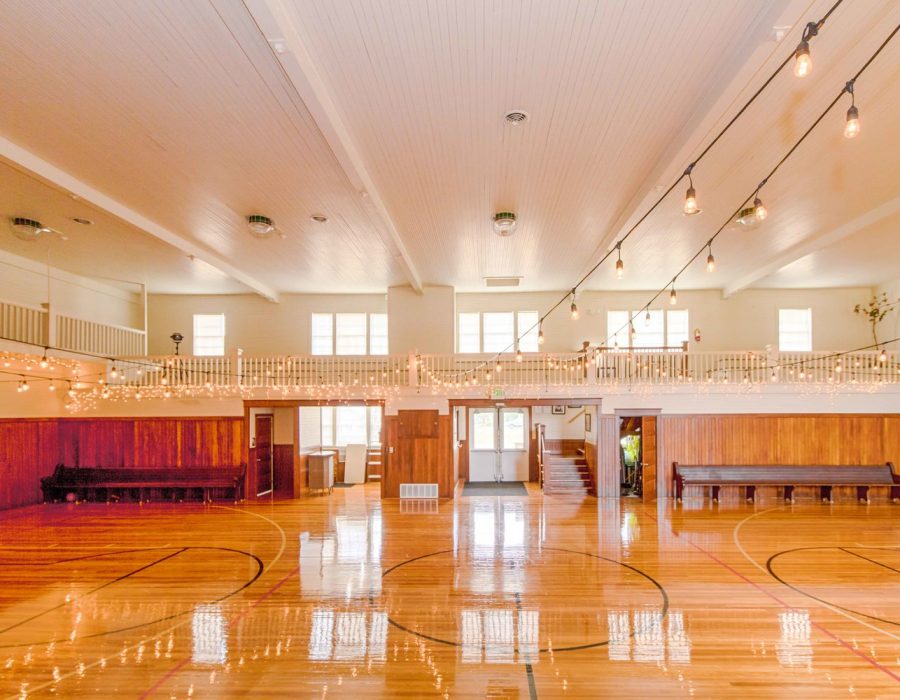 An image of the Chinok Event Center interior, showcasing bright hardwood floors and lights strung from the rafters.