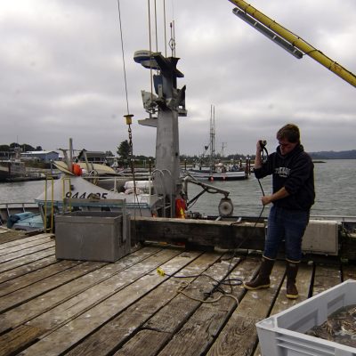 An image of a young man on the back of a crabbing ship, winding a length of cord around his arm.