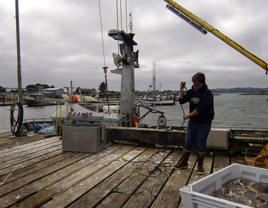 An image of a young man on the back of a crabbing ship, winding a length of cord around his arm.
