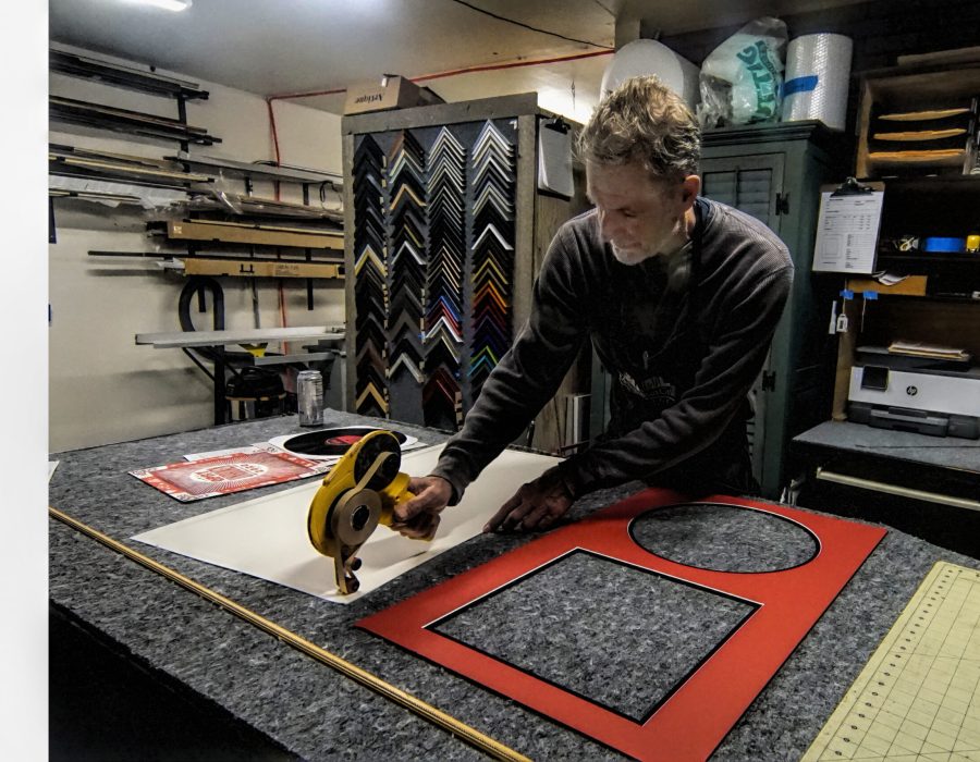 An image of a man bent over a layout table, working on framing a picture.