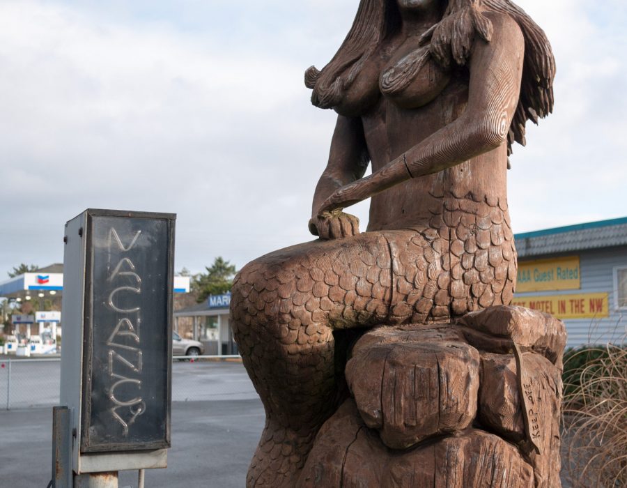 An Image of a mermaid carved out of wood that sits on the shoreline of Long Beach.