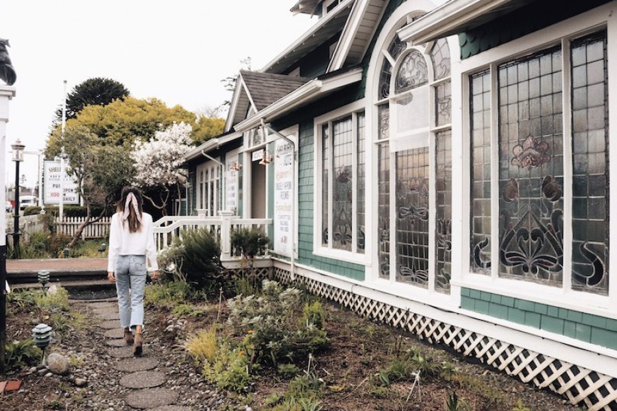 An image of a house in Seaview with pristine white trim and teal siding with woman walking in her garden out front.