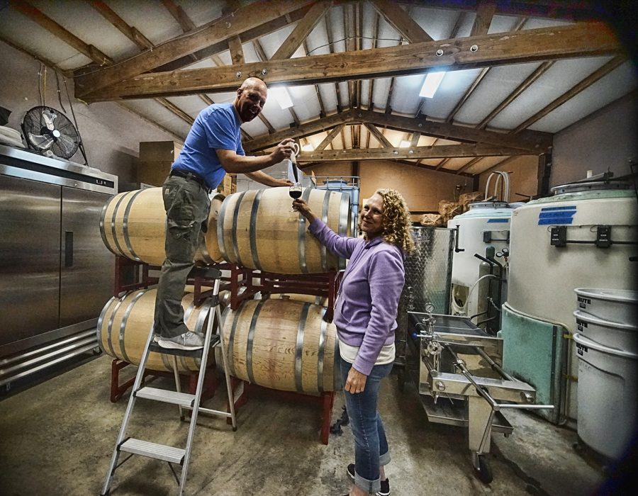 An image of the Woohoo Winery owners as they post in front of their barrels of wine.